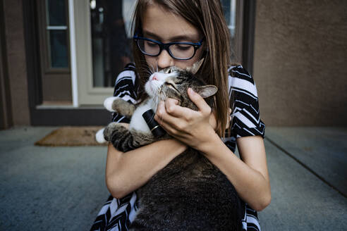 A pre teen girl kissing her cat on the front porch - CAVF89507