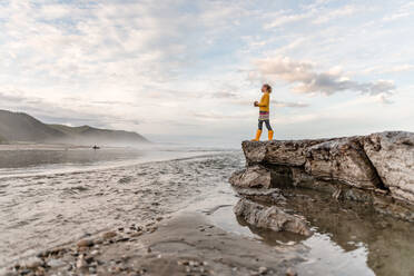 Pre-teen girl standing on rock at beach in New Zealand - CAVF89522