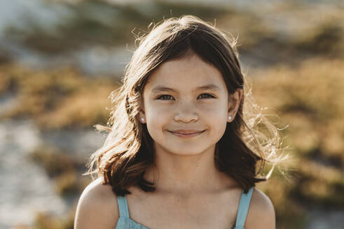Smiling 8 yr old girl with sunlight playing through her dark hair - CAVF89554