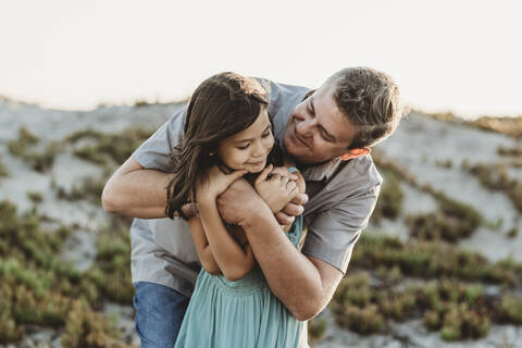 Smiling mid-40's dad hugging young daughter near sand dune stock photo