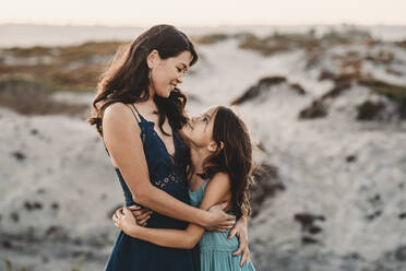 Happy mother hugging 8 yr old daughter at the beach - CAVF89582