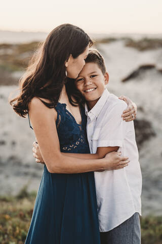 Beautiful mom tenderly embracing handsome preteen son at the beach stock photo