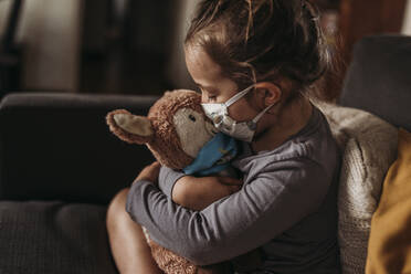 Close up of young girl with mask on kissing masked stuffed animal - CAVF89604