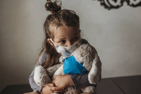 Close up of young girl with mask on kissing masked stuffed animal - CAVF89607