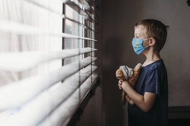 Seitenansicht eines Jungen im Schulalter mit Maske und Stofftier - CAVF89608