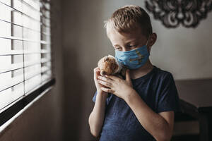 Close up of young school aged boy with mask on with stuffed animal - CAVF89610