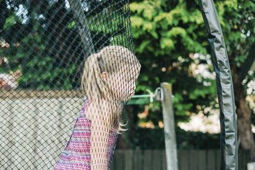 Young girl with grumpy face leaning on trampoline netting - CAVF89647