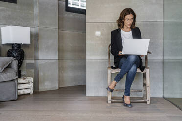 Geschäftsfrau arbeitet am Laptop, während sie auf einem Stuhl im Büro sitzt - DLTSF01232