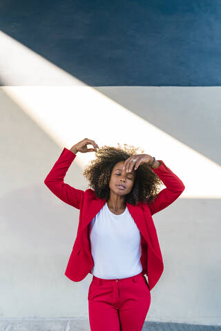 Mid adult woman standing with hand raised against wall stock photo