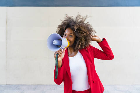 Mid adult woman using megaphone while standing against wall stock photo