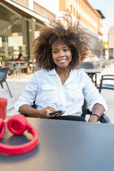 Mid adult woman using smart phone while sitting at sidewalk cafe - MGIF01008