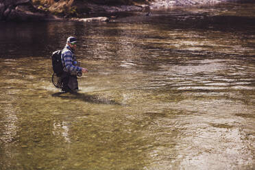 Mid adult fisherman catching fish from river on sunny day - DHEF00409