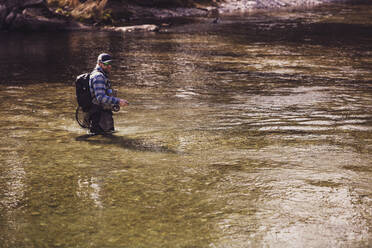 Mittlerer Erwachsener Angler, der an einem sonnigen Tag Fische aus dem Fluss fängt - DHEF00409