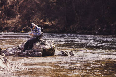 Mittlerer erwachsener Mann auf einem Felsen im Fluss sitzend an einem sonnigen Tag - DHEF00412