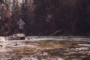 Mid adult man standing on rock catching fish from river - DHEF00413