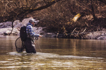 Fisherman standing in river catching fish on sunny day - DHEF00414