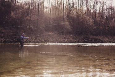 Fly fisherman throwing fishing reel in river during sunset - DHEF00416