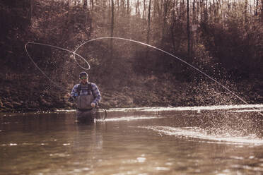 Mid adult man throwing fishing reel in river to catch fish during sunset - DHEF00418