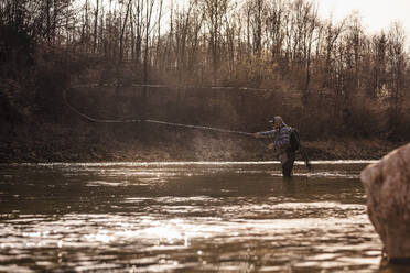 Man throwing fishing reel in river to catch fish during sunset - DHEF00419