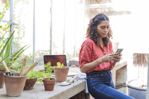 Reife Frau, die in einem Gartenhaus stehend eine SMS auf ihrem Smartphone schreibt - FMOF01098