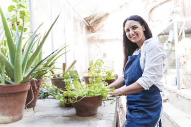 Smiling mature woman using laptop while standing in garden shed - FMOF01101