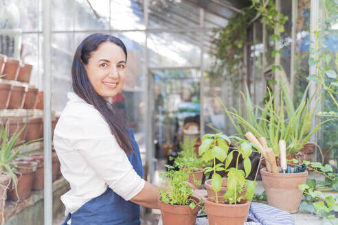 Lächelnde Frau pflanzt im Gartenhaus stehend - FMOF01103