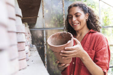 Smiling woman holding pot while standing in garden shed - FMOF01108