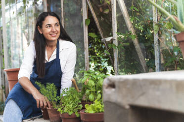 Lächelnde Frau, die in einem Gartenhaus sitzt und wegschaut - FMOF01139