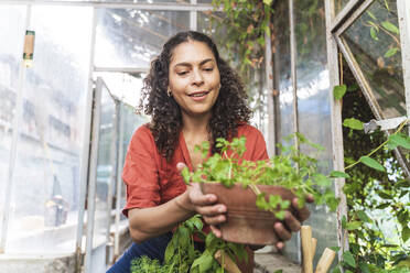 Woman holding plant while sitting in garden shed - FMOF01145