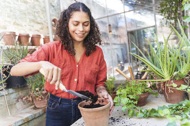 Reife Frau, die im Gartenhaus stehend Erde einbringt - FMOF01149