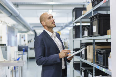 Mature male professional with digital tablet looking at containers on rack in industry - MOEF03277