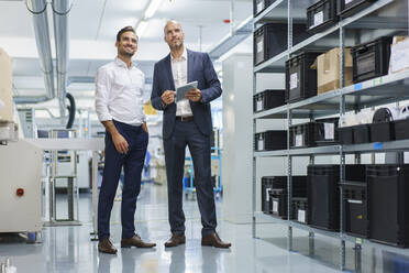 Businessman holding digital tablet while standing by smiling engineer and looking away at factory - MOEF03278