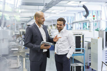 Confident businessman discussing with engineer over digital tablet at factory - MOEF03291