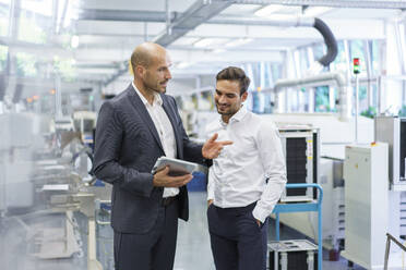 Selbstbewusster Geschäftsmann diskutiert mit einem Ingenieur über ein digitales Tablet in einer Fabrik - MOEF03291