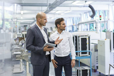 Confident male colleagues discussing while looking away at factory - MOEF03294