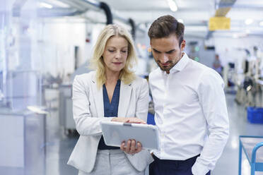 Confident blond businesswoman discussing over digital tablet with male colleague at factory - MOEF03296