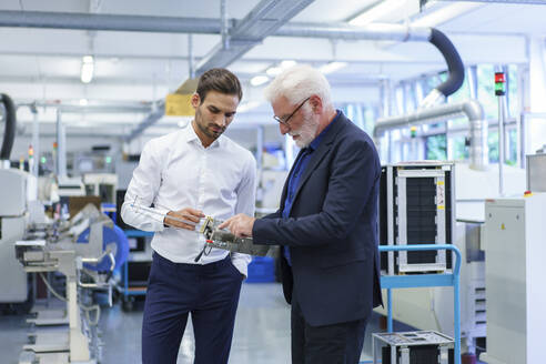 Ein leitender Angestellter zeigt auf ein Maschinenteil, während er mit einem Ingenieur an einer Maschine in einer Fabrik diskutiert - MOEF03311