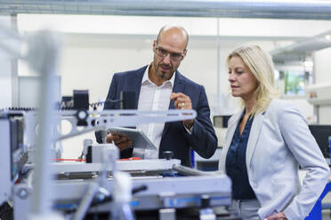 Confident businessman and businesswoman discussing while looking at machinery in factory - MOEF03336