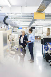 Junger Ingenieur im Gespräch mit reifer Geschäftsfrau, während er an einer Maschine in einer Fabrik steht - MOEF03343