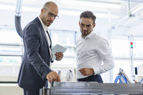 Confident male professionals discussing over machinery against machinery at factory stock photo