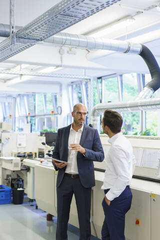 Male businessmen discussing while standing by machinery at factory stock photo