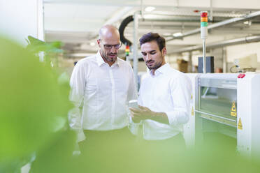 Confident male technicians discussing over remote control while standing by machinery at factory - MOEF03371