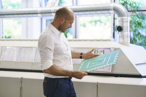 Confident mature male engineer examining large circuit board by machinery at factory stock photo