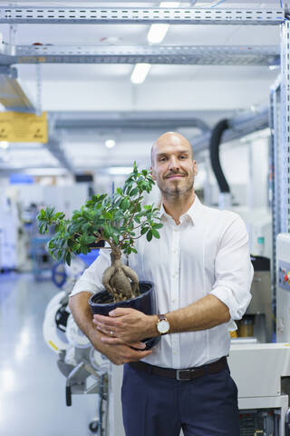 Selbstbewusster männlicher Fachmann, der eine Topfpflanze hält, während er in einer Fabrik steht, lizenzfreies Stockfoto