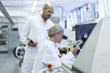 Männlicher Techniker steht neben einer Wissenschaftlerin, die in ein Mikroskop schaut, während sie im Labor forscht - MOEF03390