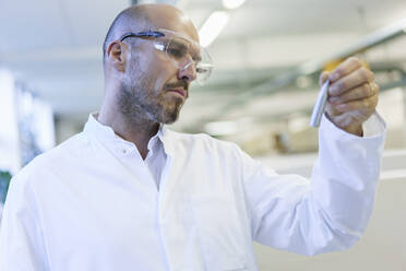 Mature male technician wearing protective eyewear looking at sample in factory - MOEF03397