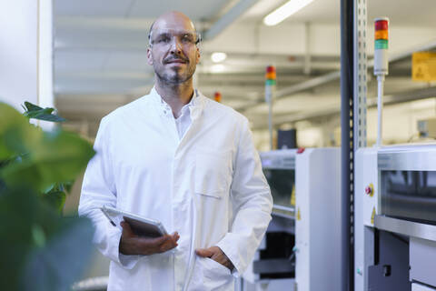 Confident male technician holding digital tablet while standing with hand in pocket at factory stock photo