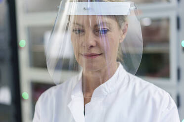 Close-up of mature female scientist wearing protective face shield at laboratory - MOEF03400