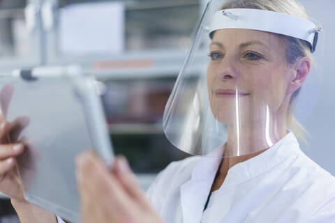 Mature female scientist wearing protective face shield while using digital tablet at laboratory stock photo