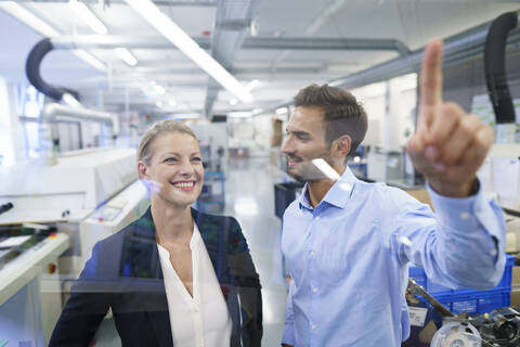 Junger männlicher Techniker, der auf eine grafische Oberfläche auf einem Glas in einer Fabrik zeigt, lizenzfreies Stockfoto